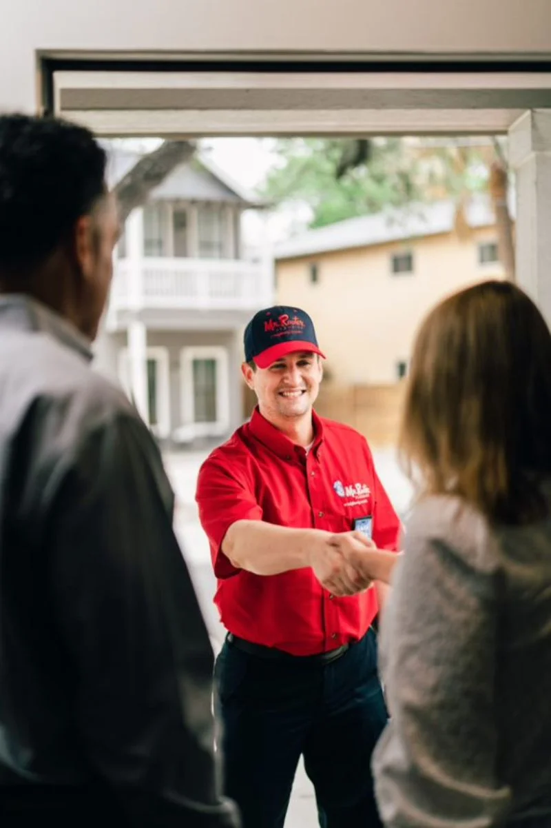 Smiling Mr. Rooter plumber greeting two customers at their front door and shaking hands with woman.