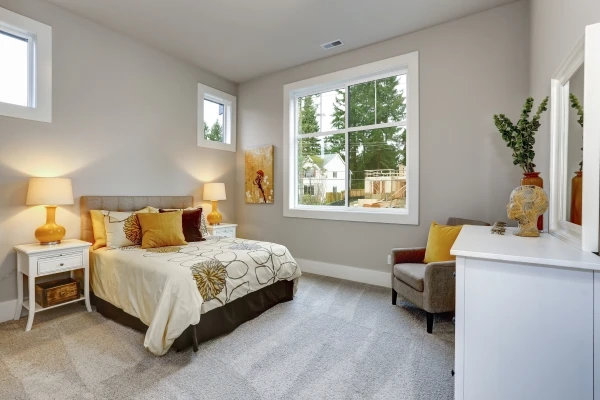 Interior of a bedroom with grey walls and carpet, with brown and yellow pillows in a guest house.