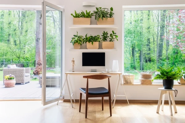 Zen home office with computer and desk in a beautiful, spacious living room interior with plants and view of outside through big windows