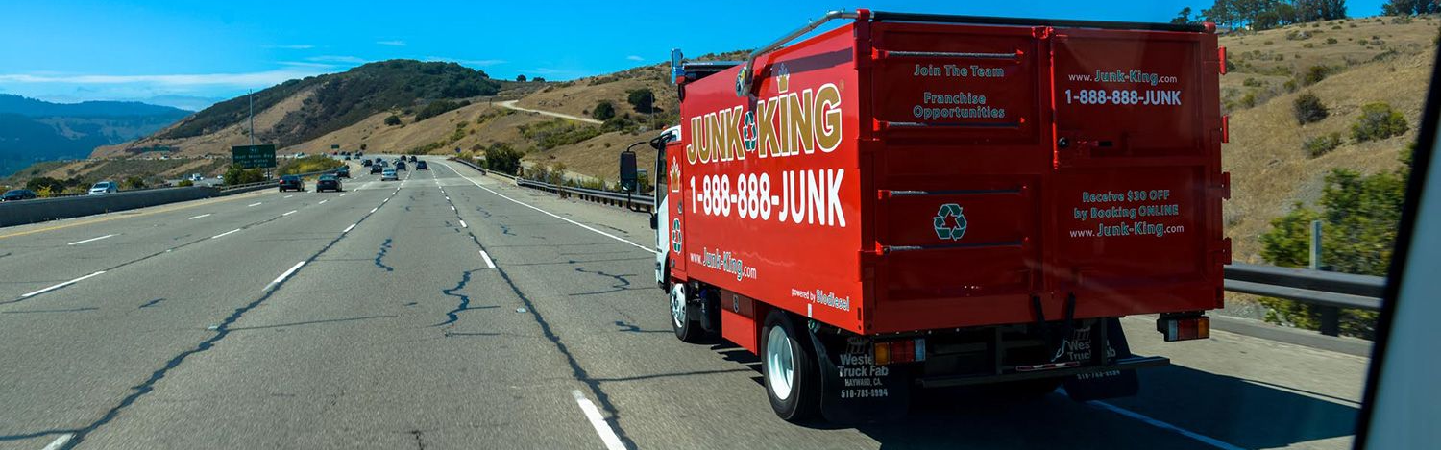 Junk King truck driving on a road with mountains in the distance.