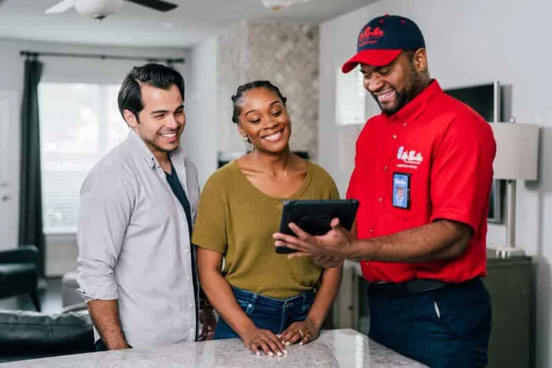 Mr. Rooter plumber showing customers options for water heater repair on tablet in customers' kitchen.