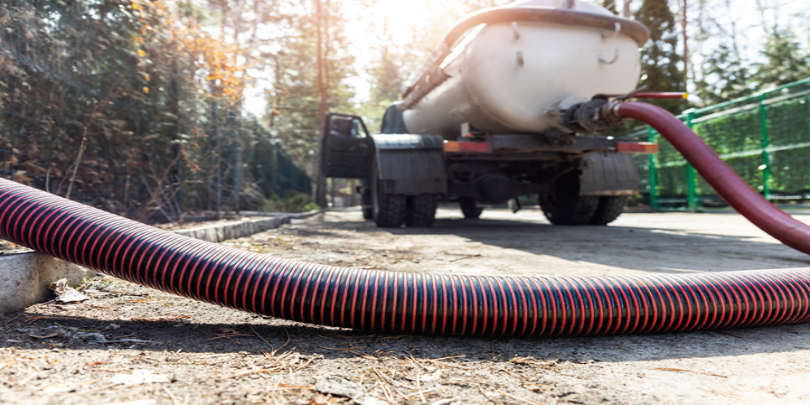 A sewage truck with its hose extended, emptying a septic tank.