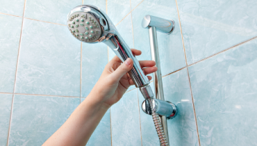 A close-up of a human hand holding a wall-mounted handheld shower head with height adjustable bar slider rail.