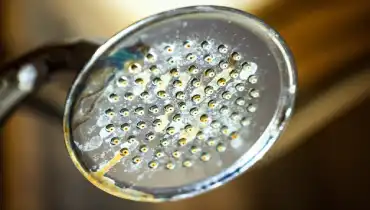 A chrome shower head with hard water deposit and rust stains from limescale.