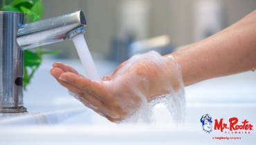 Soapy hands cupped under the stream of water coming from a stainless steel faucet.