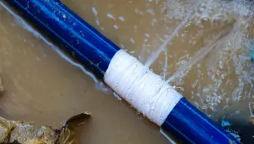 A burst pipe in a pit filled with water from the jet of water shooting out of the pipe.