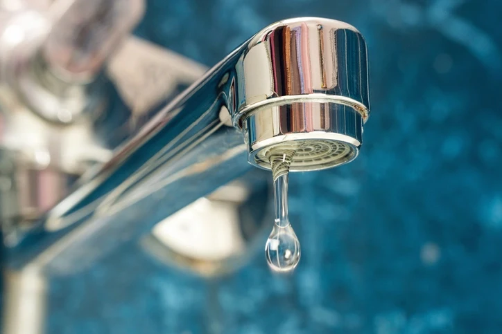 A close-up of a silver faucet with a small drop of water flowing out.