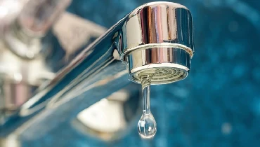 A close-up of a silver faucet with a small drop of water flowing out.