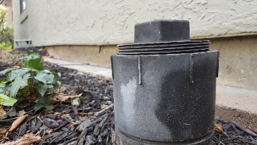 A grey sewer line cleanout on a bed of wood chips