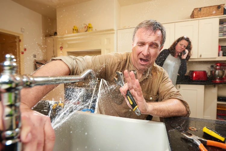 Water sprays on a homeowner attempting to fix their kitchen sink faucet.