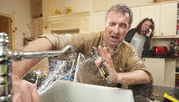 Water sprays on a homeowner attempting to fix their kitchen sink faucet.