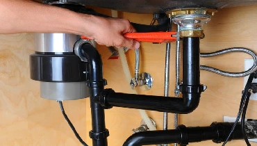 A man uses a monkey wrench to adjust a fitting on a garbage disposal underneath a kitchen sink. | Mr. Rooter Plumbing of South Jersey