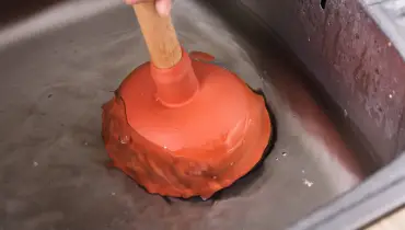 A plumber using a cup plunger to unclog a clogged sink in Dallas, TX.