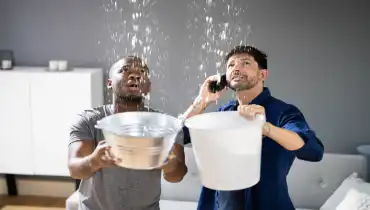 Roommates holding buckets to catch water from a ceiling leak | Mr. Rooter Plumbing of South Jersey