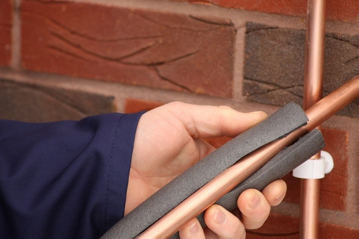 A plumber wraps foam insulation around a copper pipe. | Mr. Rooter® Plumbing of Yavapai, Coconino, and Maricopa Counties