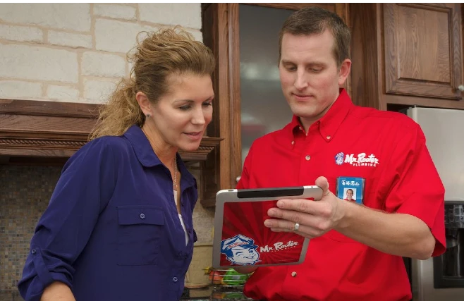 A plumber dressed in the Mr. Rooter Plumbing uniform discussing a quote for plumbing service with a homeowner.