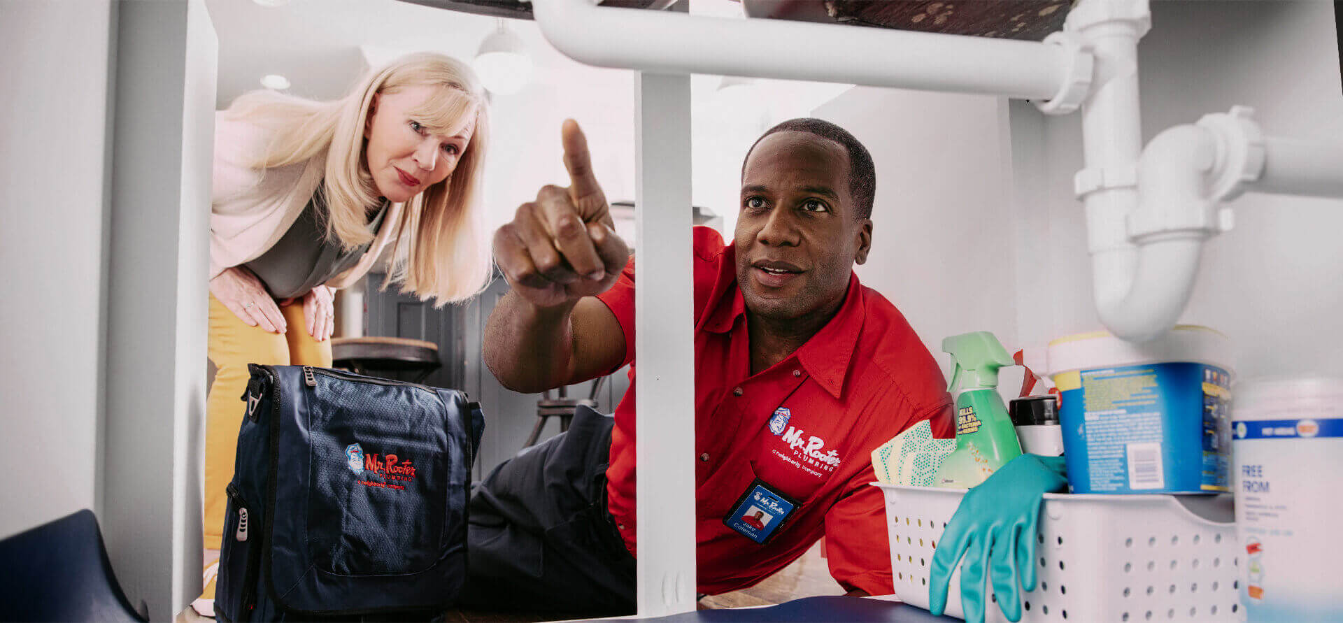 Mr. Rooter plumber looking at the kitchen sink drain and pointing something out to a customer 