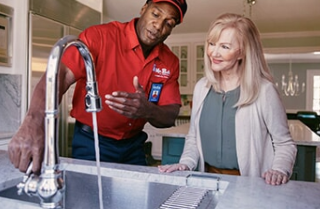 Mr. Rooter plumber showing kitchen sink faucet to homeowner.