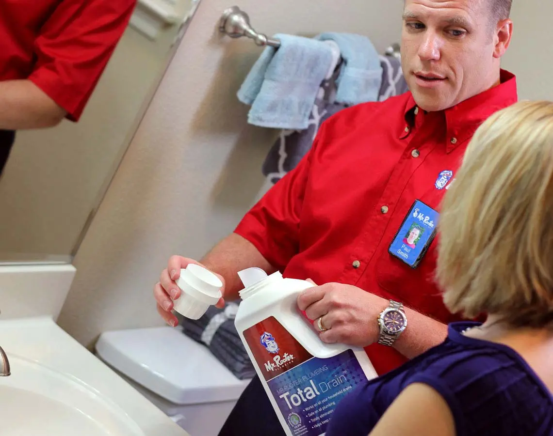 Mr. Rooter Technician talking to a customer while performing repairs on a bathroom sink.