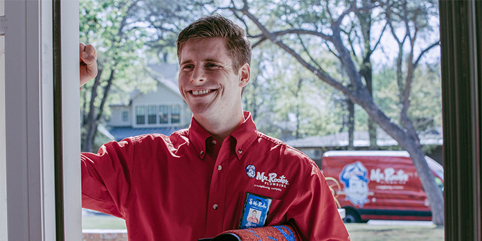 Mr. Rooter plumber smiling and knocking on door before performing plumbing repair.