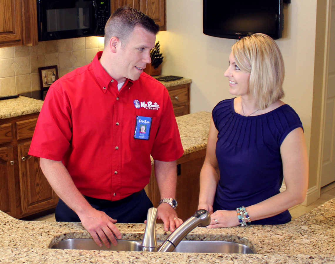 Mr. Rooter technician and customers standing at kitchen sink.