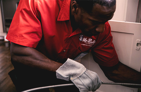 African American male Mr. Rooter handyman crouching and holding drain snake.