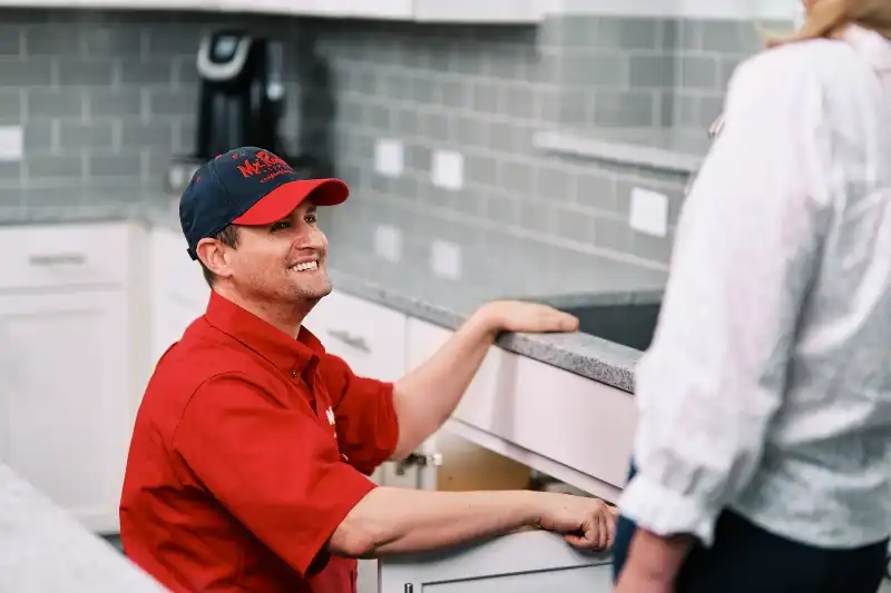 Mr. Rooter plumber crouched next to kitchen sink, smiling up at customer.