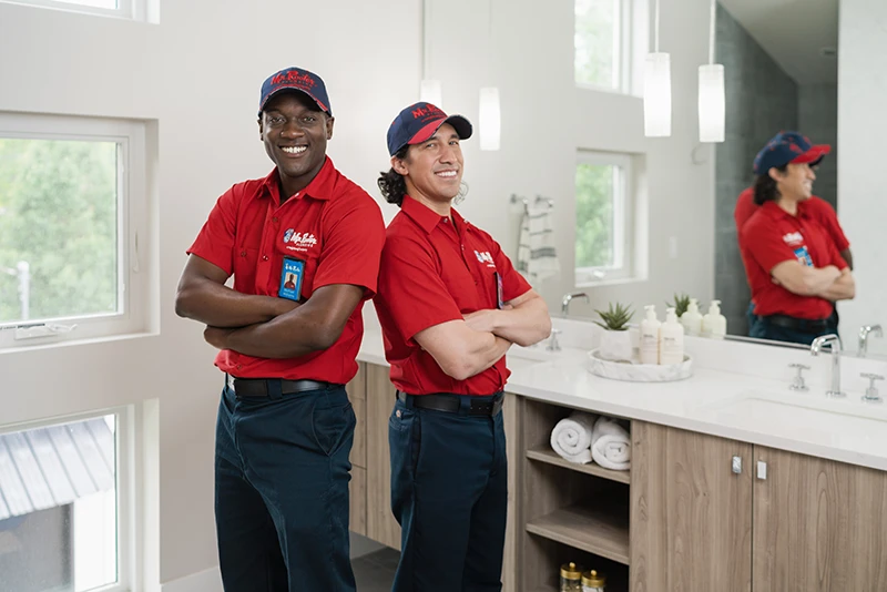 Smiling Mr. Rooter plumbers standing in a home bathroom.