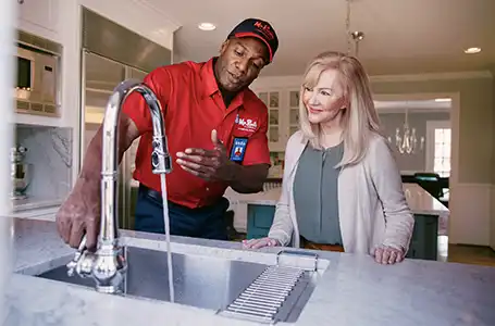 Mr. Rooter service professional turning on kitchen sink faucet to show homeowner next to him that it is working.