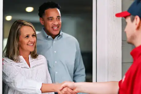 Mr. Rooter technician shaking hands with woman at front door while man looks on behind her.