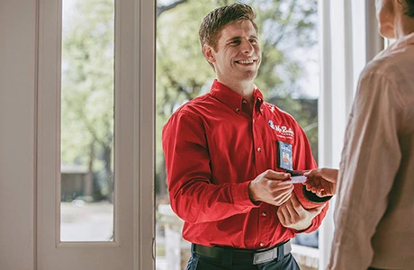 Smiling Mr. Rooter technician handing part to customer.