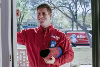 A Mr. Rooter plumber smiling and knocking on a customer's door before providing a drain cleaning service