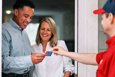 A courteous Mr. Rooter Plumbing tech handing his business card to two happy clients