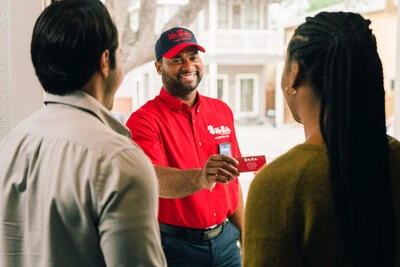 A smiling Mr. Rooter Plumbing technician showing his business card to his customers