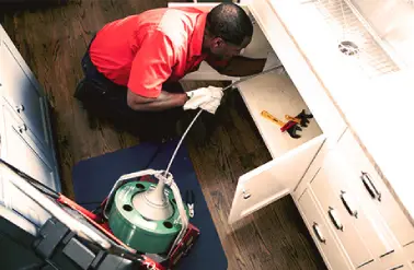 A Mr. Rooter Plumbing tech using a drain snake to clean a kitchen sink drain