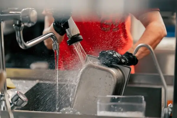 Restaurant worker cleaning off food debris for entry into commercial grease traps 