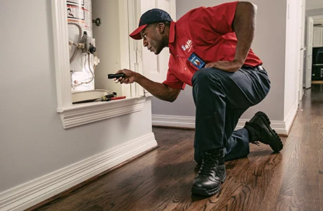 A Mr. Rooter Plumbing tech using a flashlight to inspect a water heater