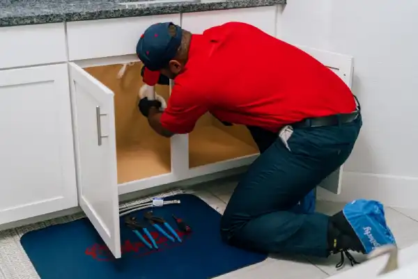 Mr. Rooter of Des Moines plumber crouching down and fixing pipes underneath sink.