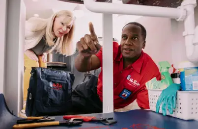 Mr. Rooter plumber pointing out something under a sink to a customer