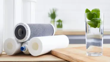 A glass of water placed next to a stack of reverse osmosis water filters."