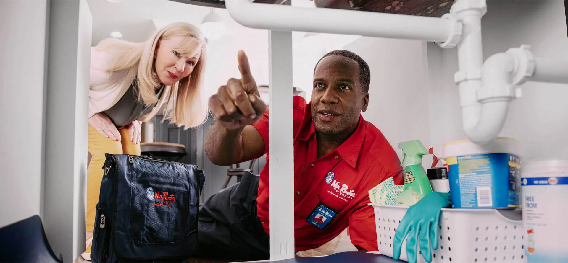 Mr. Rooter plumber in spokane pointing out something under a sink to a client