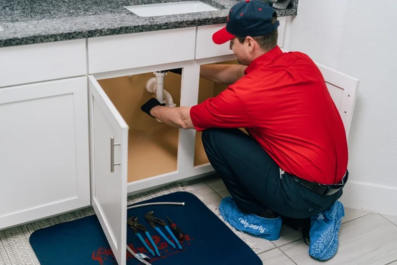 mr. rooter plumber working on a clogged drain under a sink