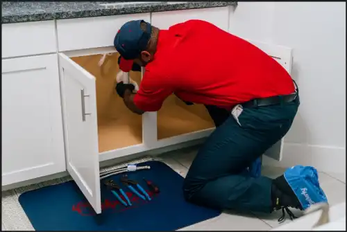 Mr. Rooter plumber crouched down and fixing under-sink plumbing.