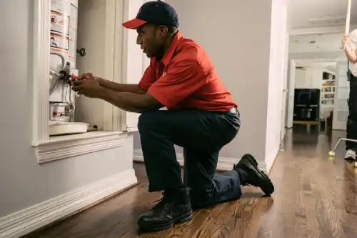 Mr. Rooter plumber fixing water heater in client's hallway.