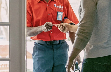 Mr. Rooter plumber handing business card to a homeowner at front door.