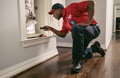 A Mr. Rooter Plumbing technician using a flashlight to inspect an in-door water heater