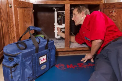 A Mr. Rooter plumber in Riverside, CA examining a pipe under a sink