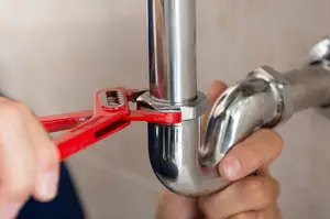 Hands fixing a pipe with a red wrench