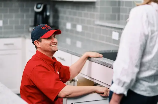 Mr. Rooter plumber explaining drain repair to the customer in a kitchen.