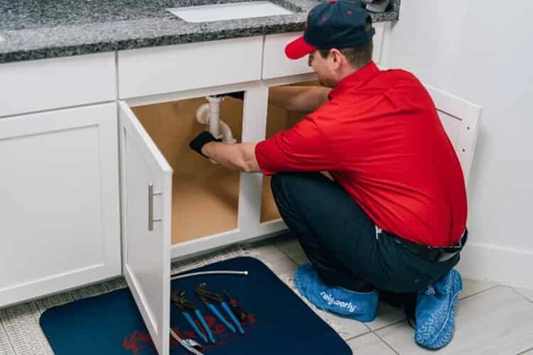 Mr. Rooter service professional working on a clogged drain under a sink